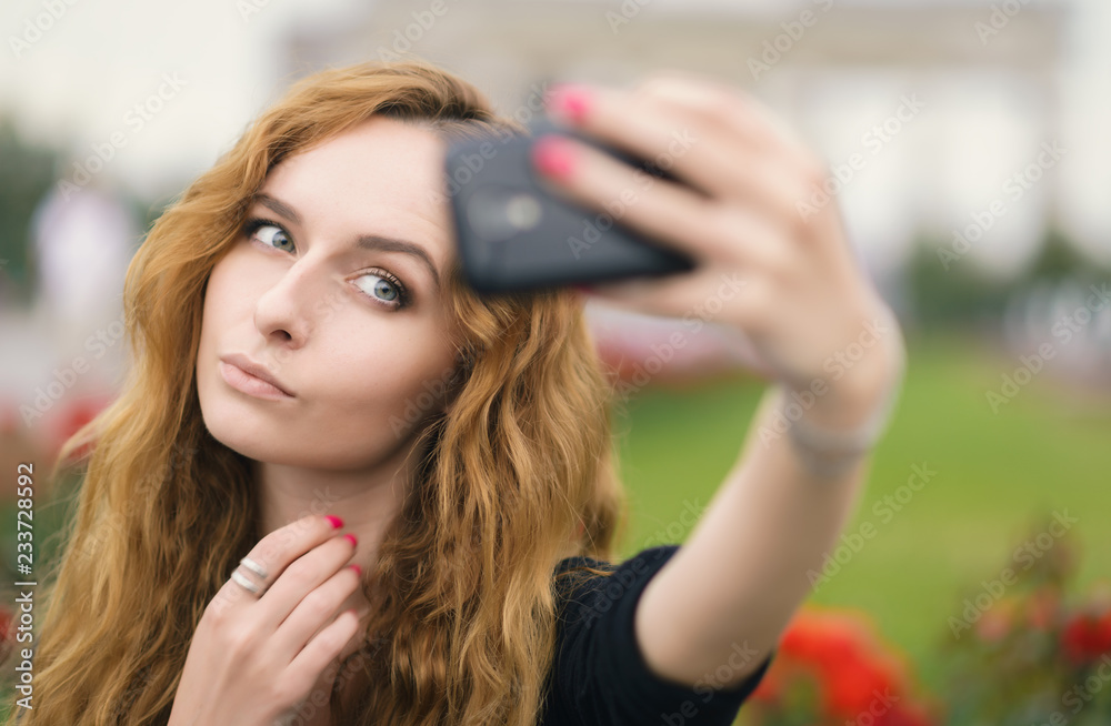 Young redhead girl taking a selfie outdoors on sunny day.