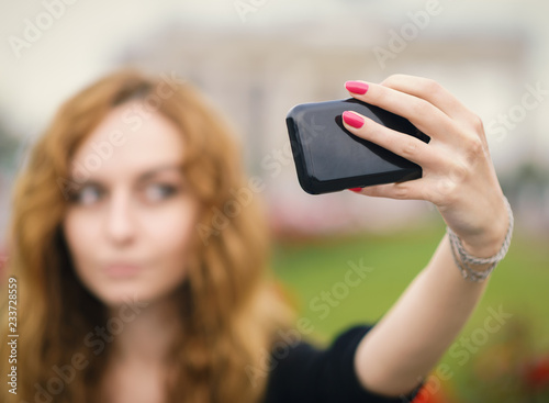 Young redhead girl taking a selfie outdoors on sunny day.