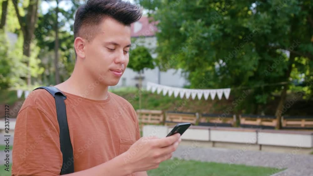 An attractive young man wearing an orange T-shirt walking and using a phone in town. Close-up dolly shot. Soft focus An attractive young man wearing an orange T-shirt walking and using a phone in town. Close-up dolly shot. Soft focus