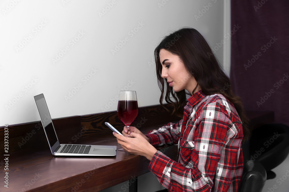Beautiful young woman with laptop and mobile phone drinking wine in bar Beautiful young woman with laptop and mobile phone drinking wine in bar