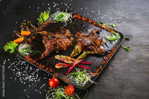 A dish with roasted quail meat with vegetables on black background