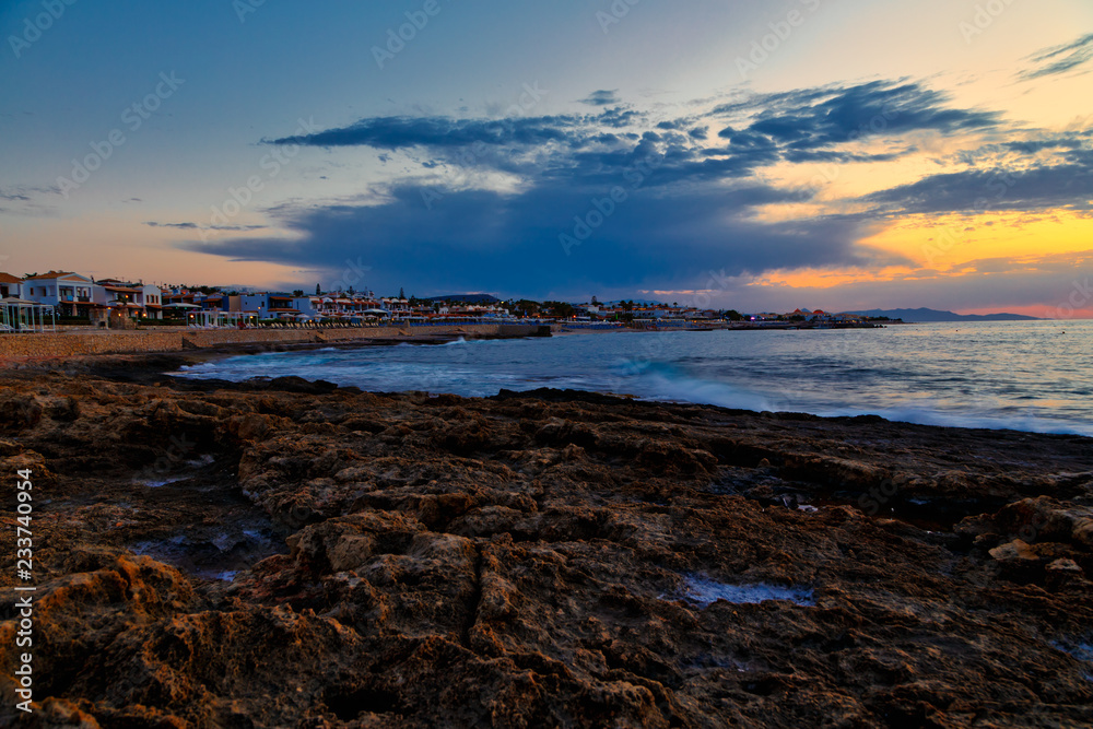 incredible sunset over the coast of Crete with hotels and beaches on the shore. Volcanic rock in the foreground