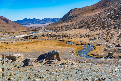 Landscape of Mongolia with the stream flowing from the snow mountain and the road from Khovd to Ulgii photo