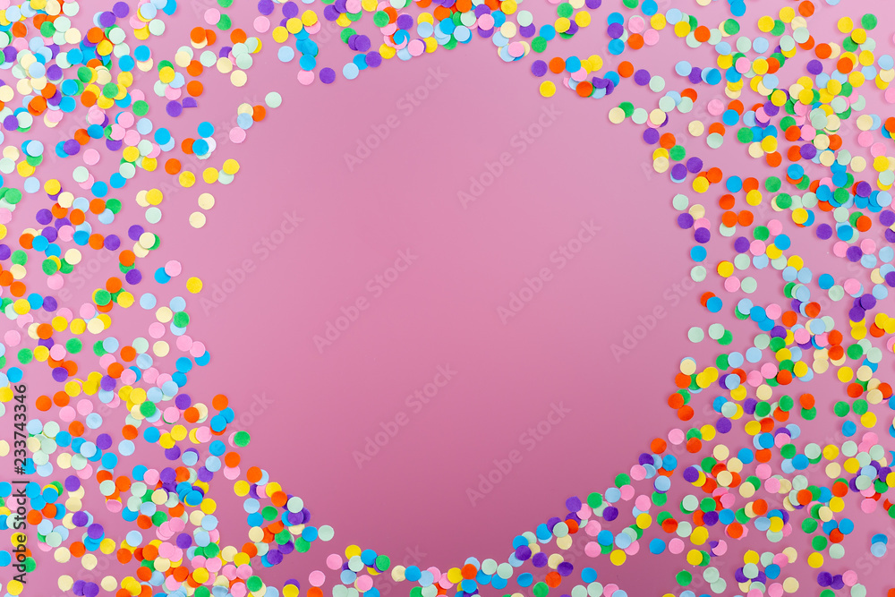 Round frame of colorful confetti on pink background.