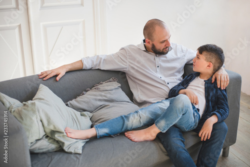 Daddy with son talking and relaxing on sofa.