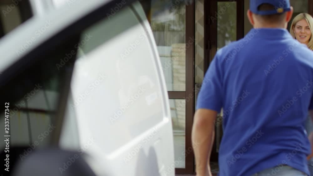 PAN shot of male courier in blue uniform getting out of delivery van and taking packages for shipping from happy woman standing on doorstep PAN shot of male courier in blue uniform getting out of delivery van and taking packages for shipping from happy woman standing on doorstep