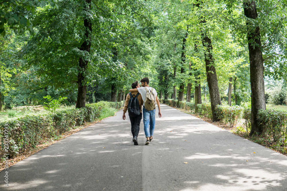 Back view of young gay couple with backpacks walking on a road Back view of young gay couple with backpacks walking on a road