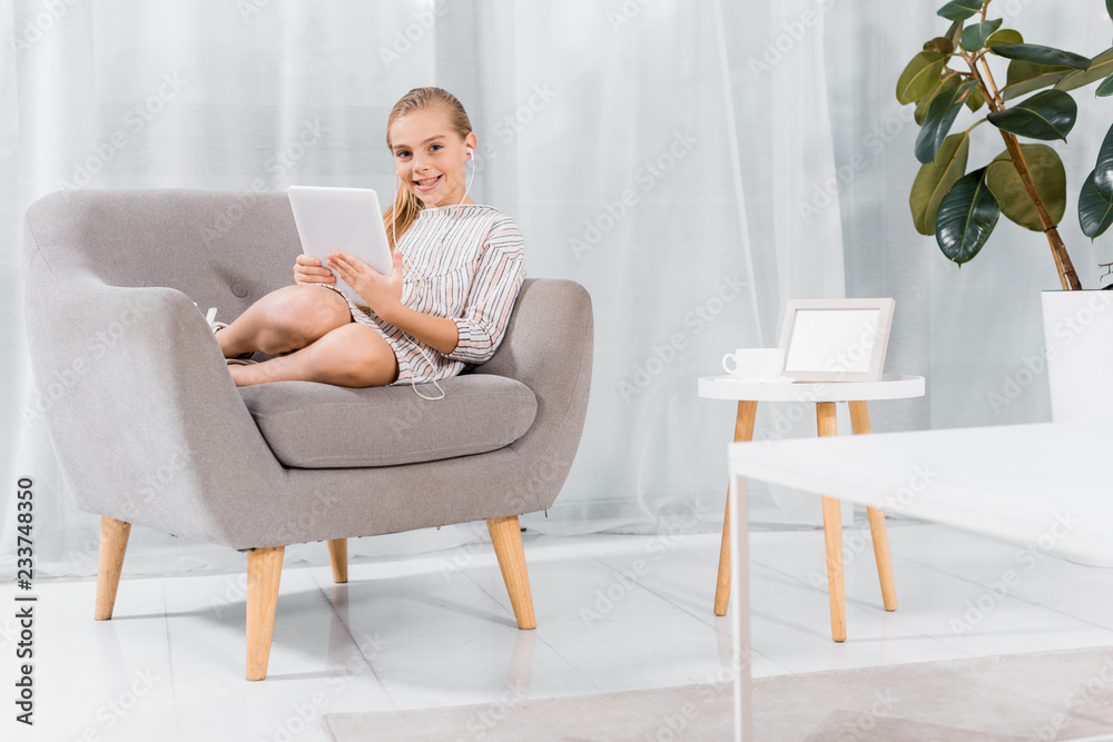 cheerful little child in earphones sitting on armchair with digital tablet at home cheerful little child in earphones sitting on armchair with digital tablet at home