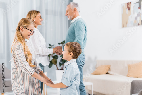 side view of mature couple holding hands of each other and their grandchildren holding hands near at home