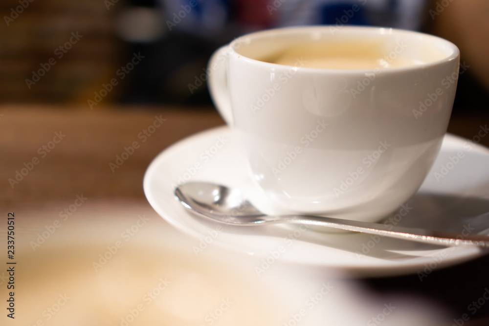 White porcelain cup of milk tea (tea with milk isolated) with teaspoon on a table (a cafe in Jimbocho, Tokyo)