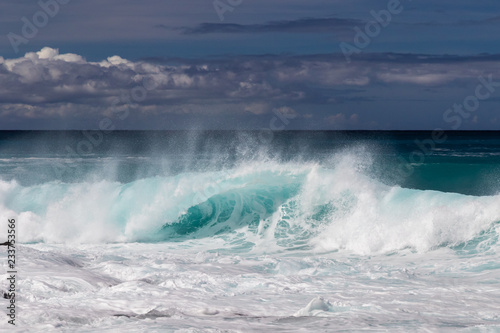 wave curling on Hawaiian beach. Spray flyng back on wave s top. From from earlier wave in foreground.  White sea spray thrown into the air. Near Kona  on Hawaii s Big Island.