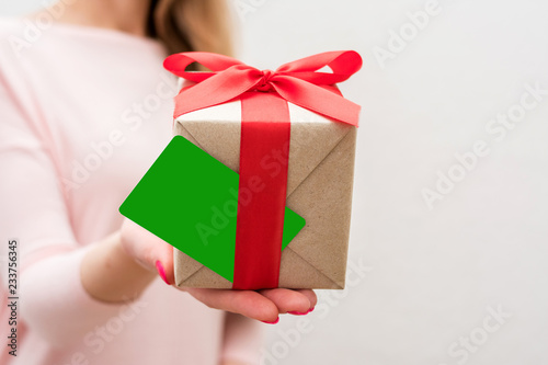 Fototapeta Naklejka Na Ścianę i Meble -  Woman holding a box with a gift, business card to the camera, front view, close up, background with copy space, for advertising or slogan