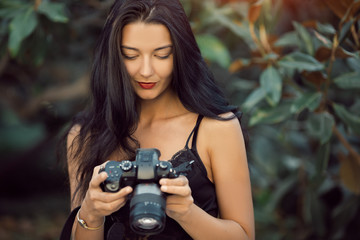 Attractive woman photographer taking images with dslr camera outdoors in park. Gorgeous happy mixed race Asian Caucasian female enjoying traveling outdoors during holidays in Europe.