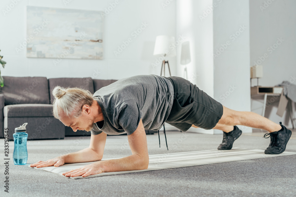 athletic man in sportswear doing plank exercise on yoga mat at home