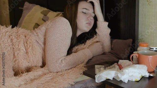The girl lies on the bed and is sick. There are antibiotics on the bedside tables. HD