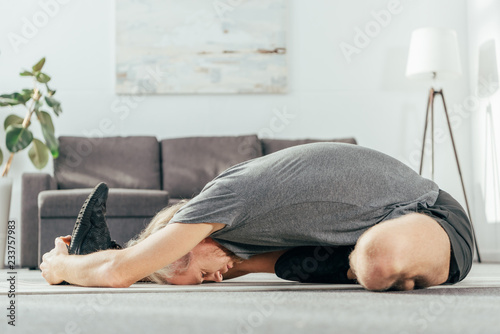 side view of athletic man in sportswear exercising and stretching on yoga mat at home