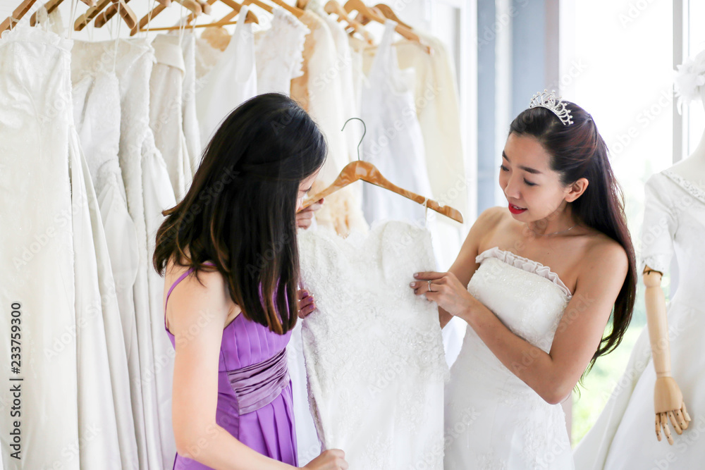 Beautiful bride getting dressed by her best friend in her wedding day and choosing a wedding dress in the shop and the shop assistant is helping her Beautiful bride getting dressed by her best friend in her wedding day and choosing a wedding dress in the shop and the shop assistant is helping her