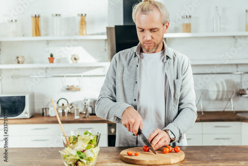 man chopping cherry tomatoes and cooking vegetable salad in kitchen