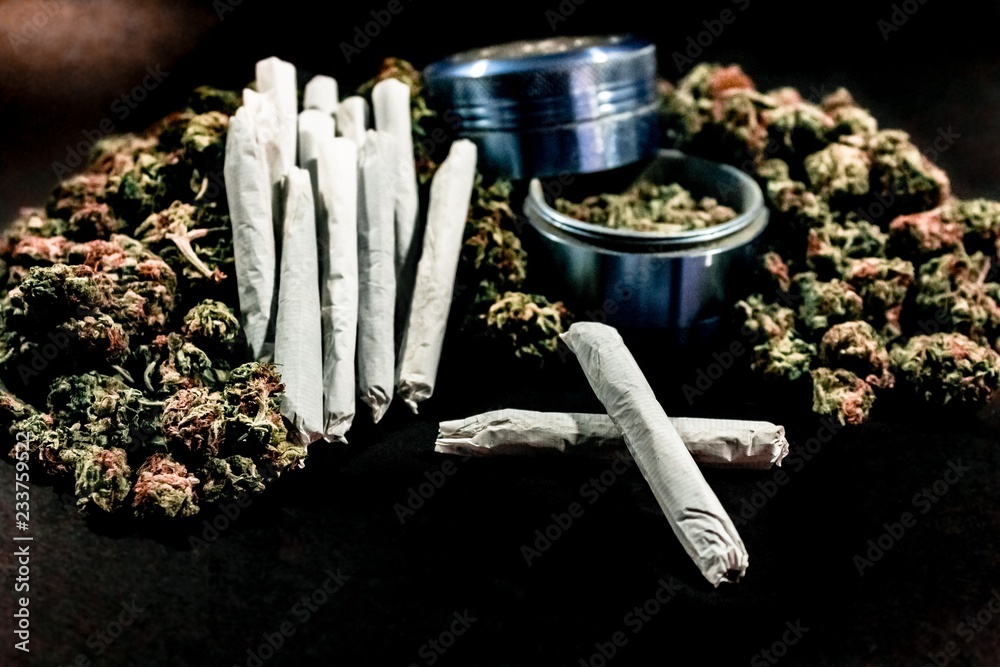 Marijuana joints stacked on a pile of bud with a cobalt coloured bud grinder.