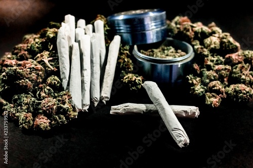 Marijuana joints stacked on a pile of bud with a cobalt coloured bud grinder.