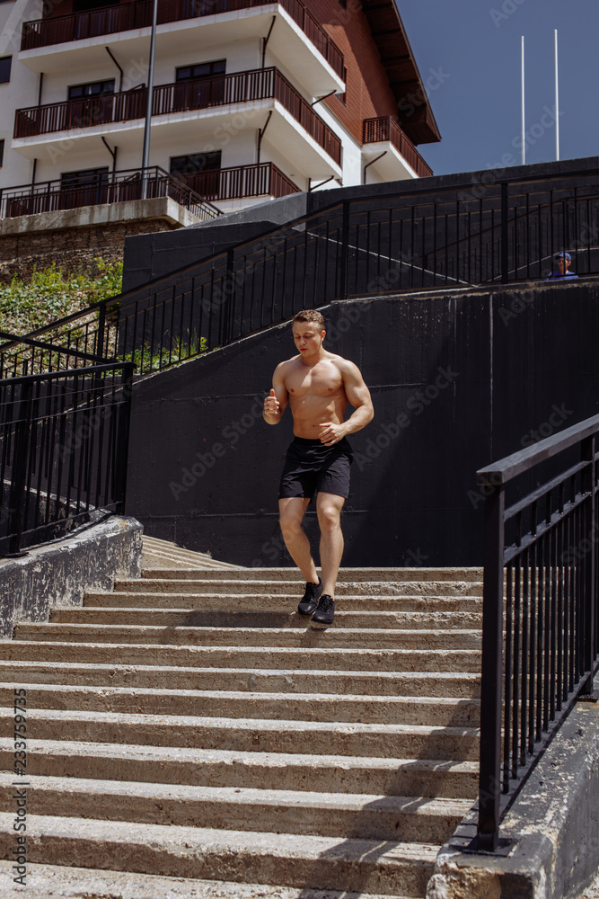 Caucasian shirtless athletic runner running up and down the stairs in the city background. Fitness, outdoor sports lifestyle concept