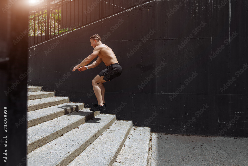 Fototapeta premium Cute caucasian shirtless jumper in motion, flying over the stairs, doing crossfit training outdoors. Healthy lifestyle, sport and people.