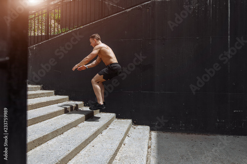 Cute caucasian shirtless jumper in motion, flying over the stairs, doing crossfit training outdoors. Healthy lifestyle, sport and people.