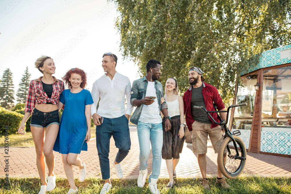 Fototapeta premium Happy multiethnic friends being glad to be together at urban park outdoors, spend leisure time in entertainment outdoor center.