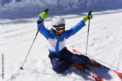 Un niño con esquís y un casco de esquí se levante de la nieve con la ayuda de bastones de esquí.