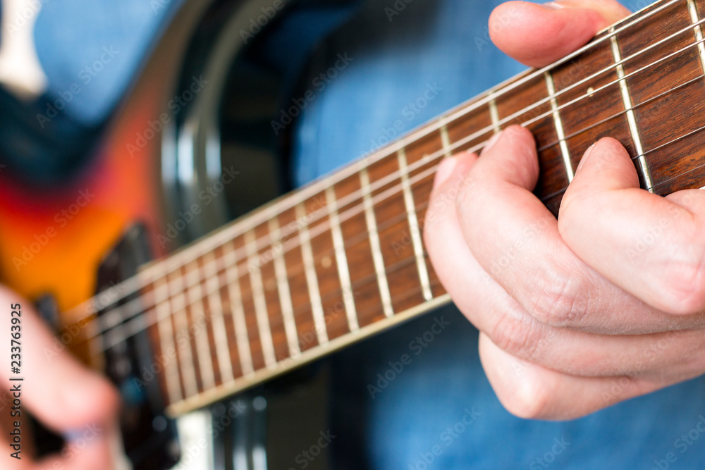 Hands of a musician in a denim shirt playing vintage sunburst guitar