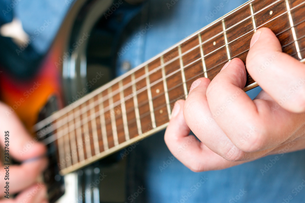 Fototapeta premium Hands of a man in a denim shirt playing vintage sunburst guitar