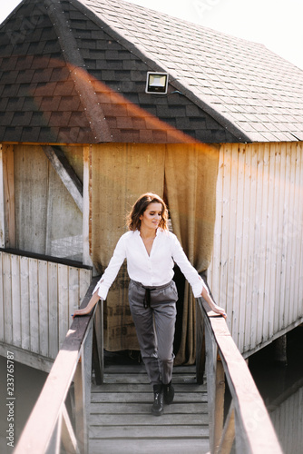 Atmospheric portrait of a beautiful lonely girl walking around a wooden house on the water at the lake © Oleksandr