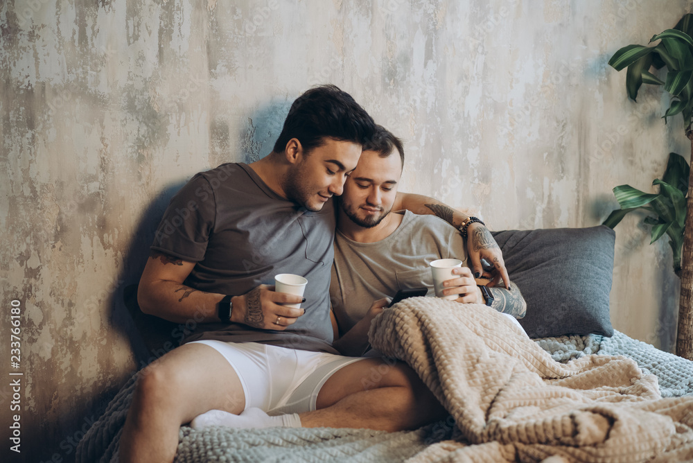 Happy alternative couple in bed drinking coffee and looking through photos rememebering last night party in the morning, bonding each other with tenderness. Happy alternative couple in bed drinking coffee and looking through photos rememebering last night party in the morning, bonding each other with tenderness.
