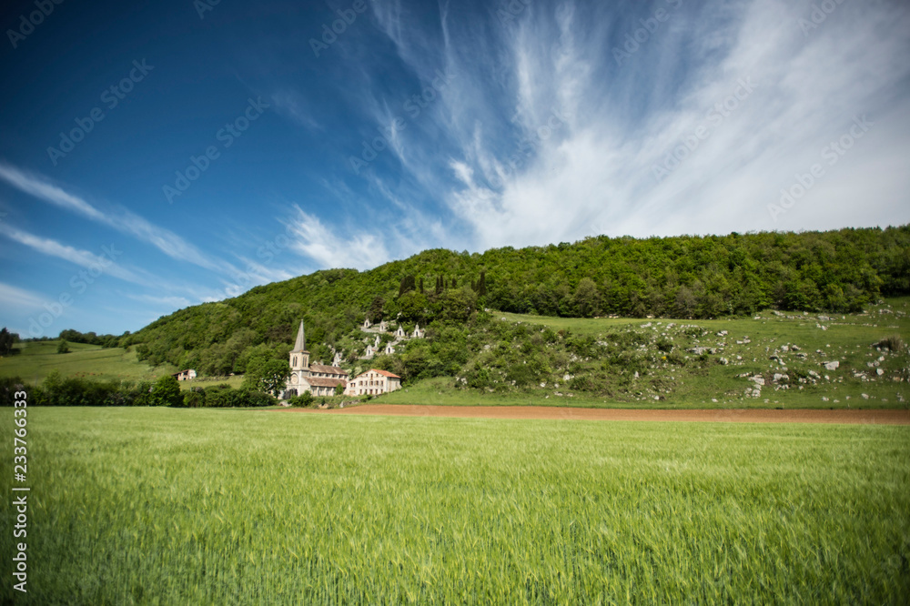 Landscape view of green fields with church and the stations of the cross on the hillside behind with blue sky and whispy clouds