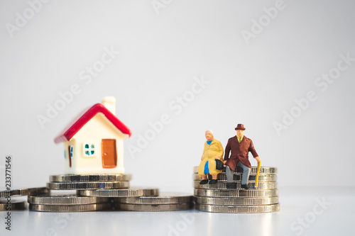Miniature elderly people sitting on stack coins and mini house using as job retirement, business and insurance concept