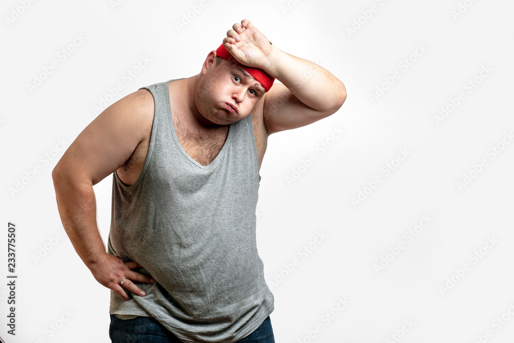 Obese unsporting non- athletic man during his training session, resting, exhausted, taking a overwork, wipes sweat with hand from his forehead against white background. I - obrazy, fototapety, plakaty 