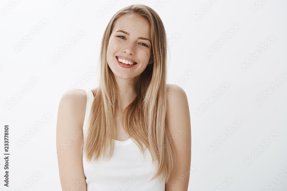 Friendly-looking sociable young woman with blond hair and perfect skin smiling broadly with white teeth at camera, tilting head gazing happily, posing over gray background delighted and self-aware Friendly-looking sociable young woman with blond hair and perfect skin smiling broadly with white teeth at camera, tilting head gazing happily, posing over gray background delighted and self-aware
