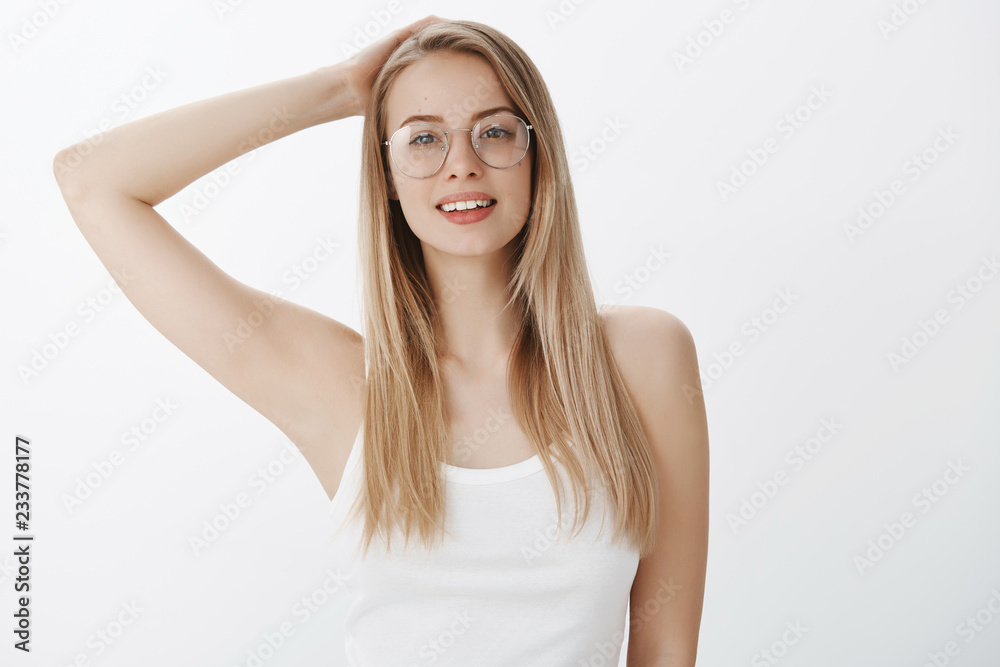 Waist-up shot of smart and relaxed good-looking young european female with fair hair and moles wearing transparent glasses holding hand behind head smiling looking calm and peaceful, enjoying weekend Waist-up shot of smart and relaxed good-looking young european female with fair hair and moles wearing transparent glasses holding hand behind head smiling looking calm and peaceful, enjoying weekend
