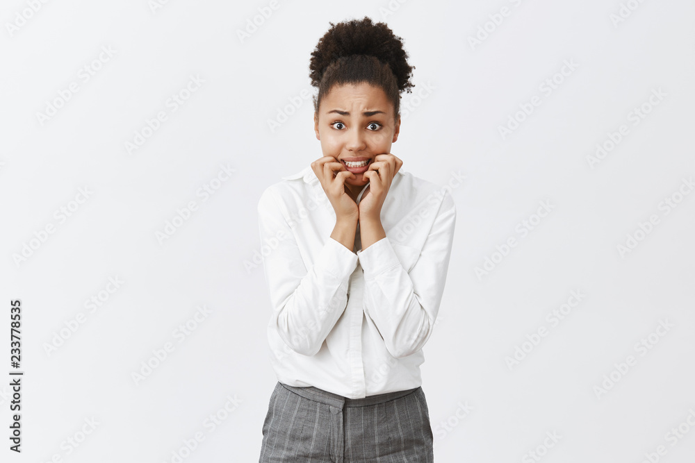 Girl stuck in elevator being scared to death, standing over gray background, biting fingernails from fear and anxiety, staring intensely at camera, waiting for rescue, wearing office pants and shirt Girl stuck in elevator being scared to death, standing over gray background, biting fingernails from fear and anxiety, staring intensely at camera, waiting for rescue, wearing office pants and shirt