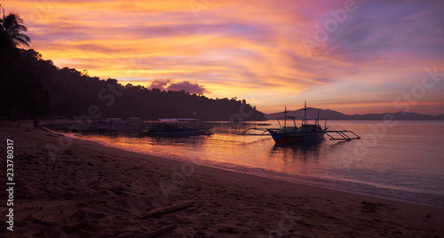Fototapeta Naklejka Na Ścianę i Meble -  Outstanding light at sunset on the beach of the tropical remote fishing village of Port Barton in Philippines, with bobbing boats on water.  Long exposure to create soft effect 