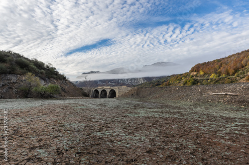 Photo of a valley with a old bridge in ruins in the reservoir of Riaño in Leon, Spain. In the background you see the mountains between the morning mists, in a cold day of the winter. photo