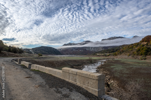 Old road over a ruined bridge that is generally flooded by the waters of the reservoir of Riaño in Leon, Spain. In the background you see the mountains between the morning mists.  photo