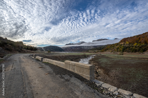 Old road over a ruined bridge that is generally flooded by the waters of the reservoir of Riaño in Leon, Spain. In the background you see the mountains between the morning mists.  photo