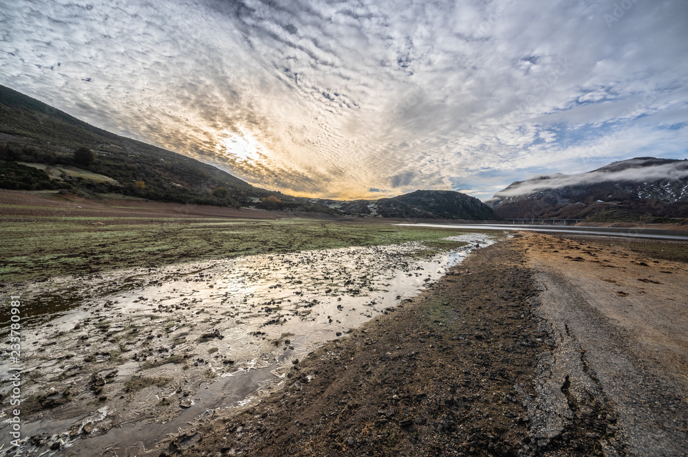 Old road in ruins that is generally flooded by the waters of the reservoir of Riaño in Leon, Spain. You see the sun among the clouds.