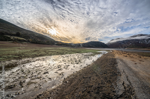 Old road in ruins that is generally flooded by the waters of the reservoir of Riaño in Leon, Spain. You see the sun among the clouds. photo