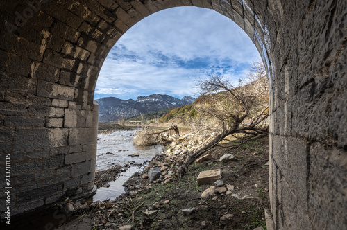 View through the arch of a bridge in ruins of the valley flooded by the riaño reservoir, in Vegacerneja, Leon (Spain). In the background you can see the mountains of the area. photo