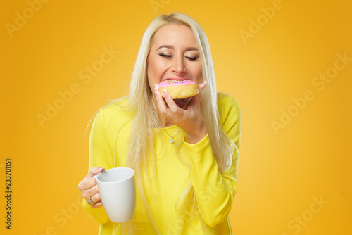 Woman holding colorful donut with sprinkles on a yellow background. Cup of coffee. Concept of food and Tasty