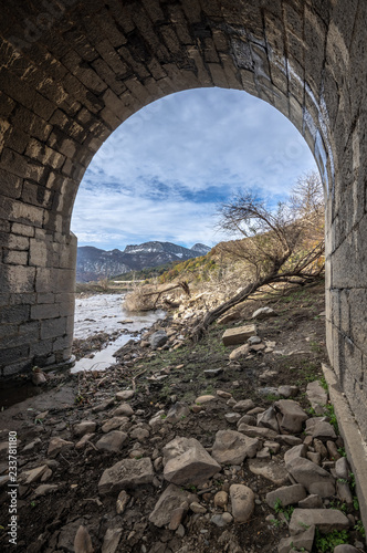 View through the arch of a bridge in ruins of the valley flooded by the riaño reservoir, in Vegacerneja, Leon (Spain). In the background you can see the mountains of the area. photo