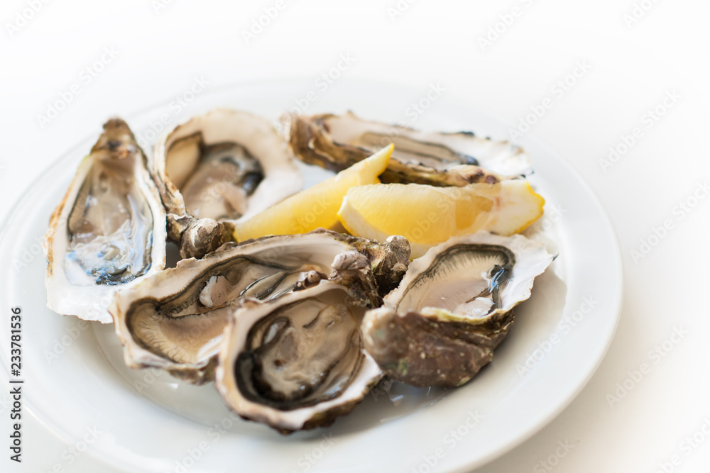Fresh oysters. Raw fresh oysters on white round plate, image isolated, with soft focus. Restaurant delicacy. Saltwater oysters Fresh oysters. Raw fresh oysters on white round plate, image isolated, with soft focus. Restaurant delicacy. Saltwater oysters