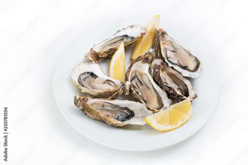 Fresh oysters. Raw fresh oysters on white round plate, image isolated, with soft focus. Restaurant delicacy. Saltwater oysters Fresh oysters. Raw fresh oysters on white round plate, image isolated, with soft focus. Restaurant delicacy. Saltwater oysters
